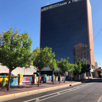 Photo of a large bank building from a distance with a small but long horizontal mural on a wall below it.
