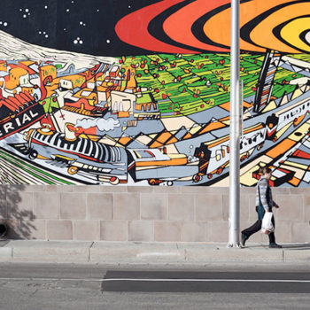 Photo of person walking infront of a colorful and fun mural of downtown Albuquerque.