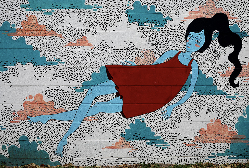 Very friendly mural of a cartoonish young woman floating in a cool dreamscape with cotton candy clouds.