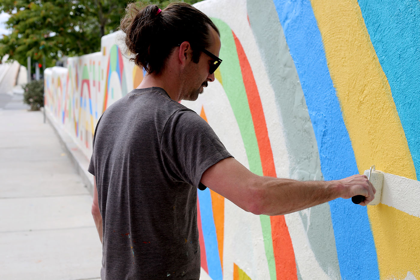Photo of the pony-tailed artist in sunglasses painting a mural in progress.