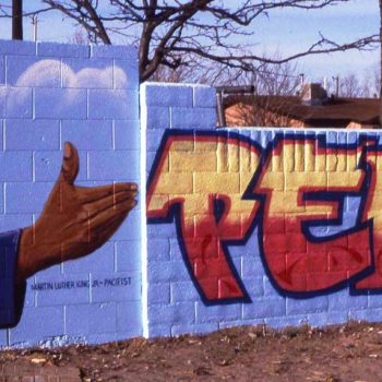 hand gesturing toward lettering painted on wall